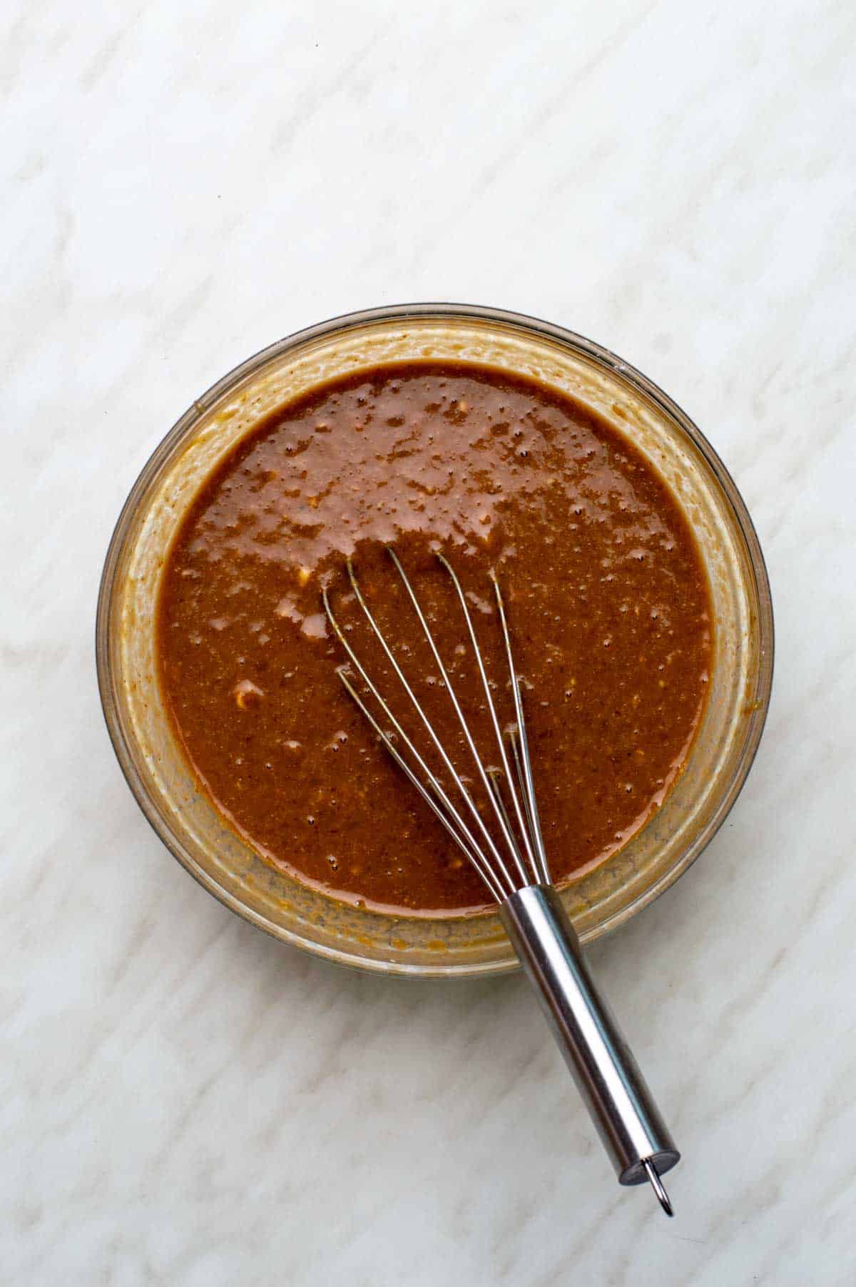 A bowl of wet banana bread ingredients all mixed together with a silver spatula resting in the bowl.