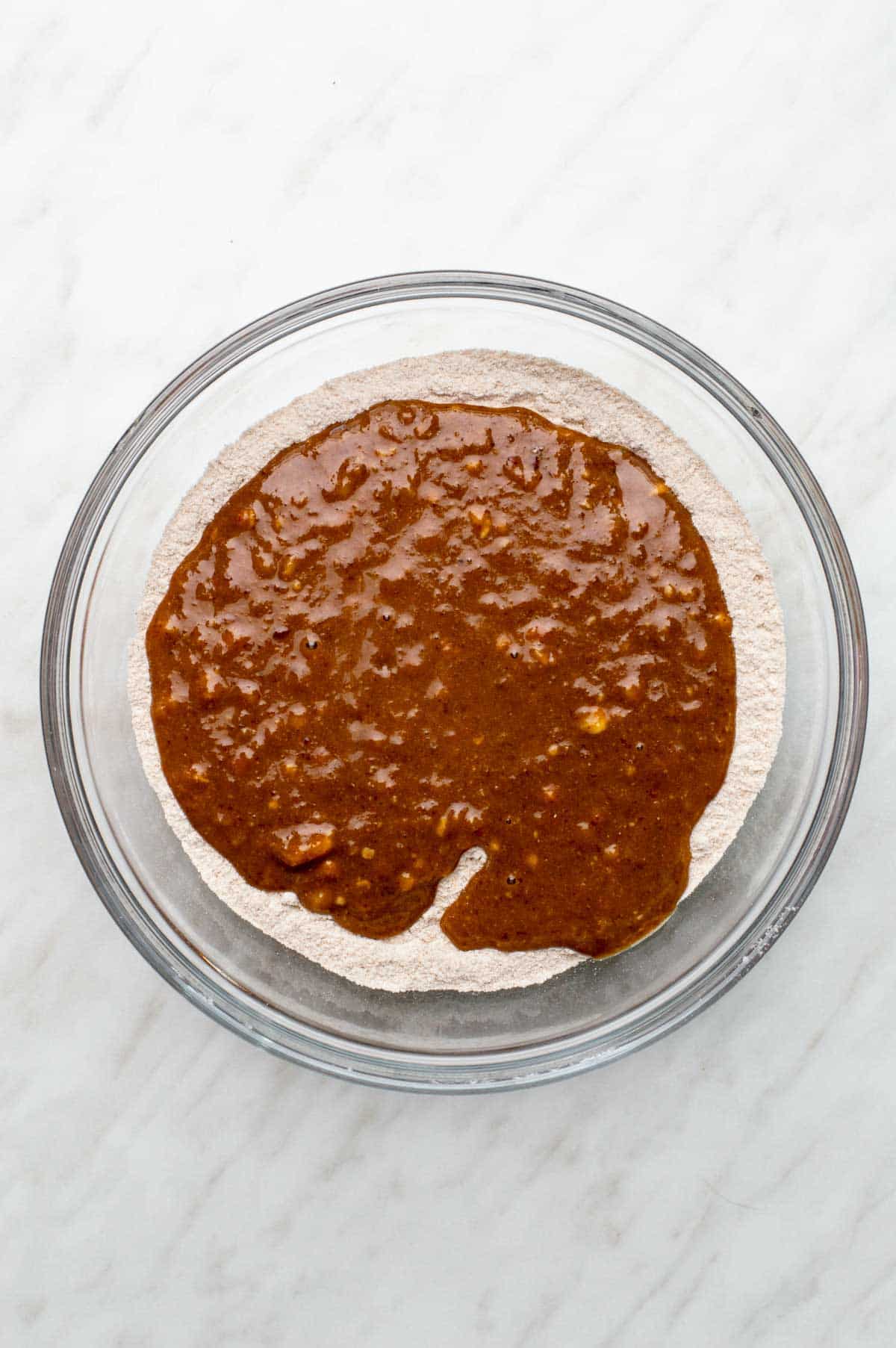 A bowl of dry ingredients with the wet banana mixture just poured on top, ready to be mixed together.