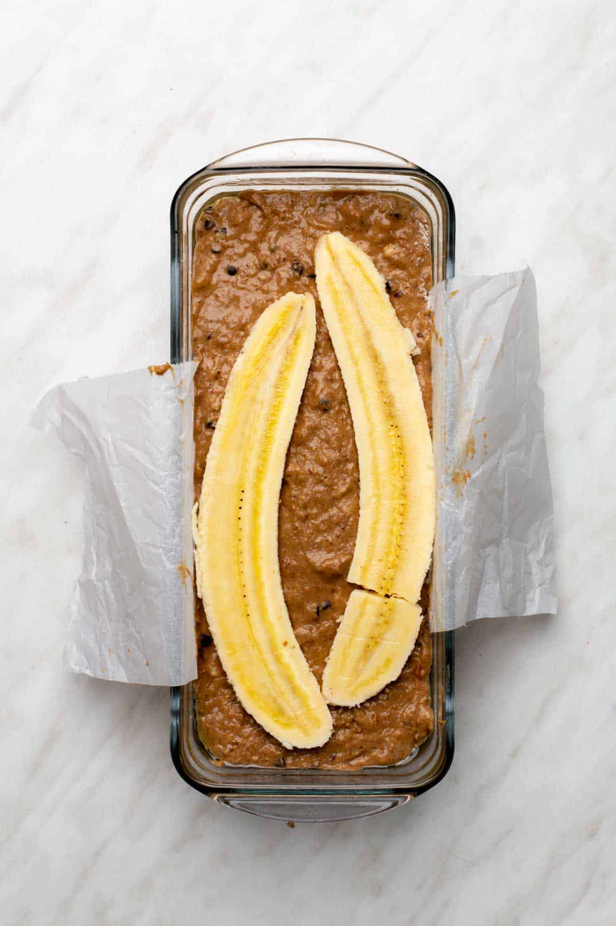 A loaf pan filled with banana bread batter and topped with lengthwise slices of banana.