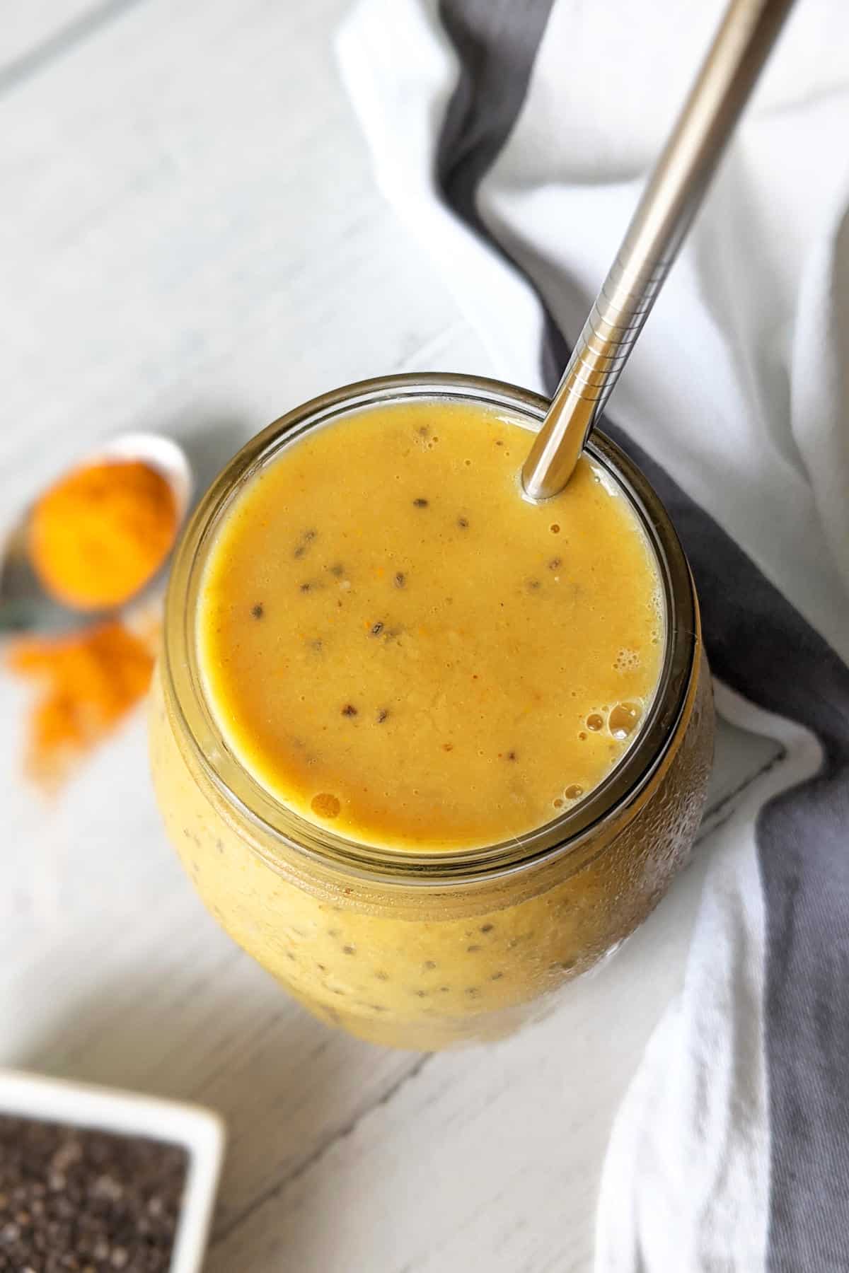 A large glass mason jar filled with maca smoothie and served with a stainless steel straw.