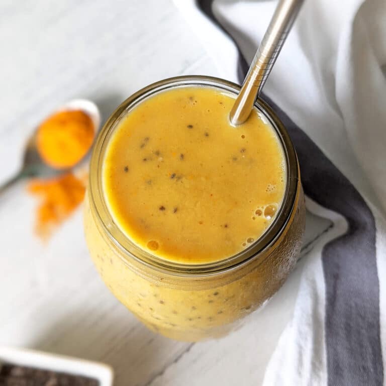A large glass mason jar filled with maca smoothie and served with a stainless steel straw.