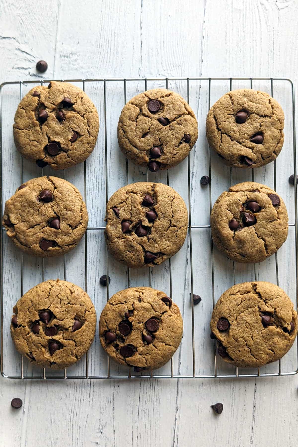 Cookies cooling on a rack with chocolate chips scattered around.