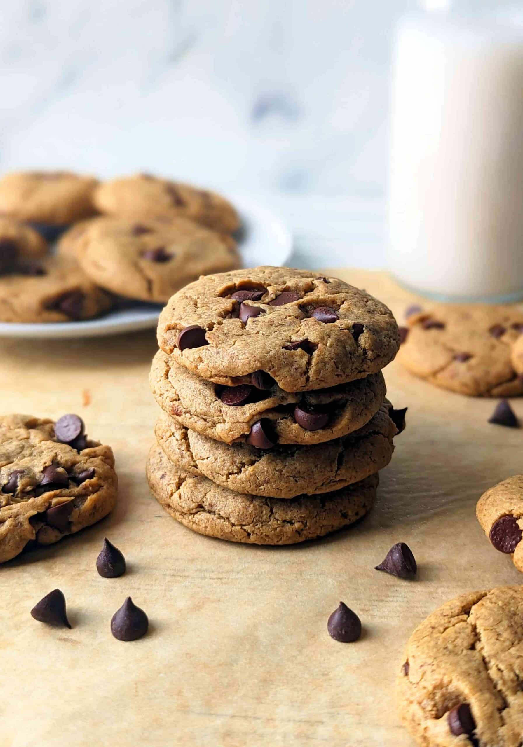 Four vegan peanut butter chocolate chip cookies stacked on one another with more cookies scattered around.