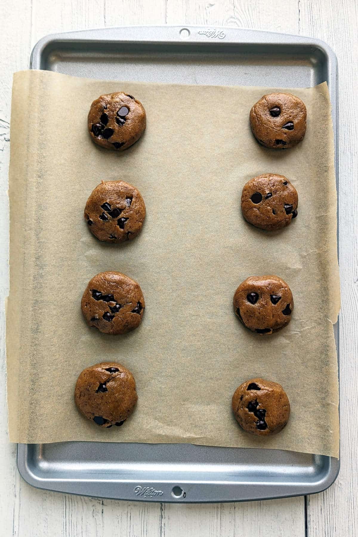 Vegan peanut butter chocolate chip cookies rolled into balls and then flattened a little on a cookie sheet.