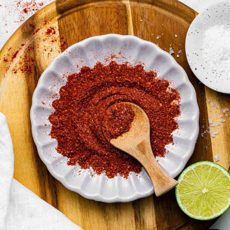 Chili lime seasoning on a small white plate with a wooden scoop and a fresh lime halved.