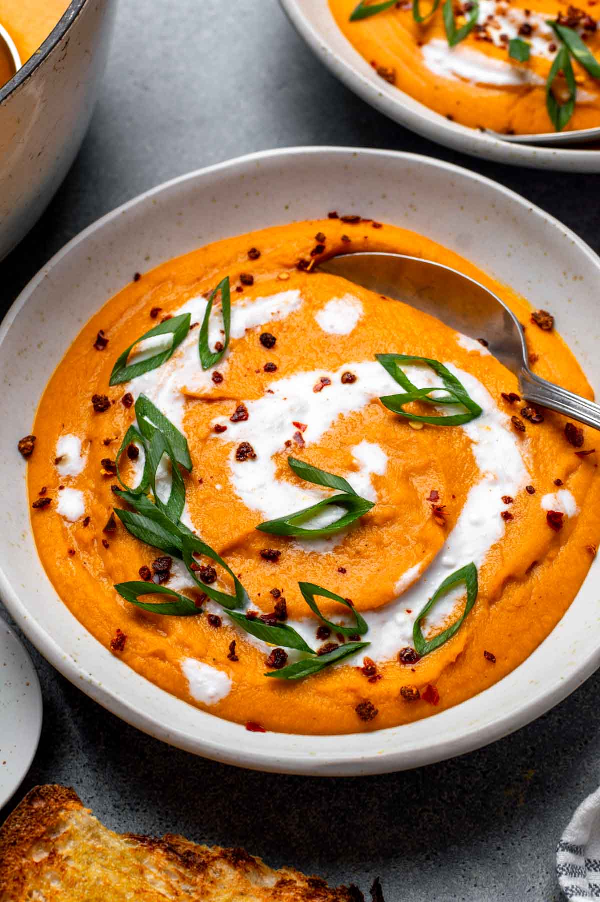 Bowl of lentil carrot soup served with a spoon and topped with a swirl of coconut milk and sliced green onions.