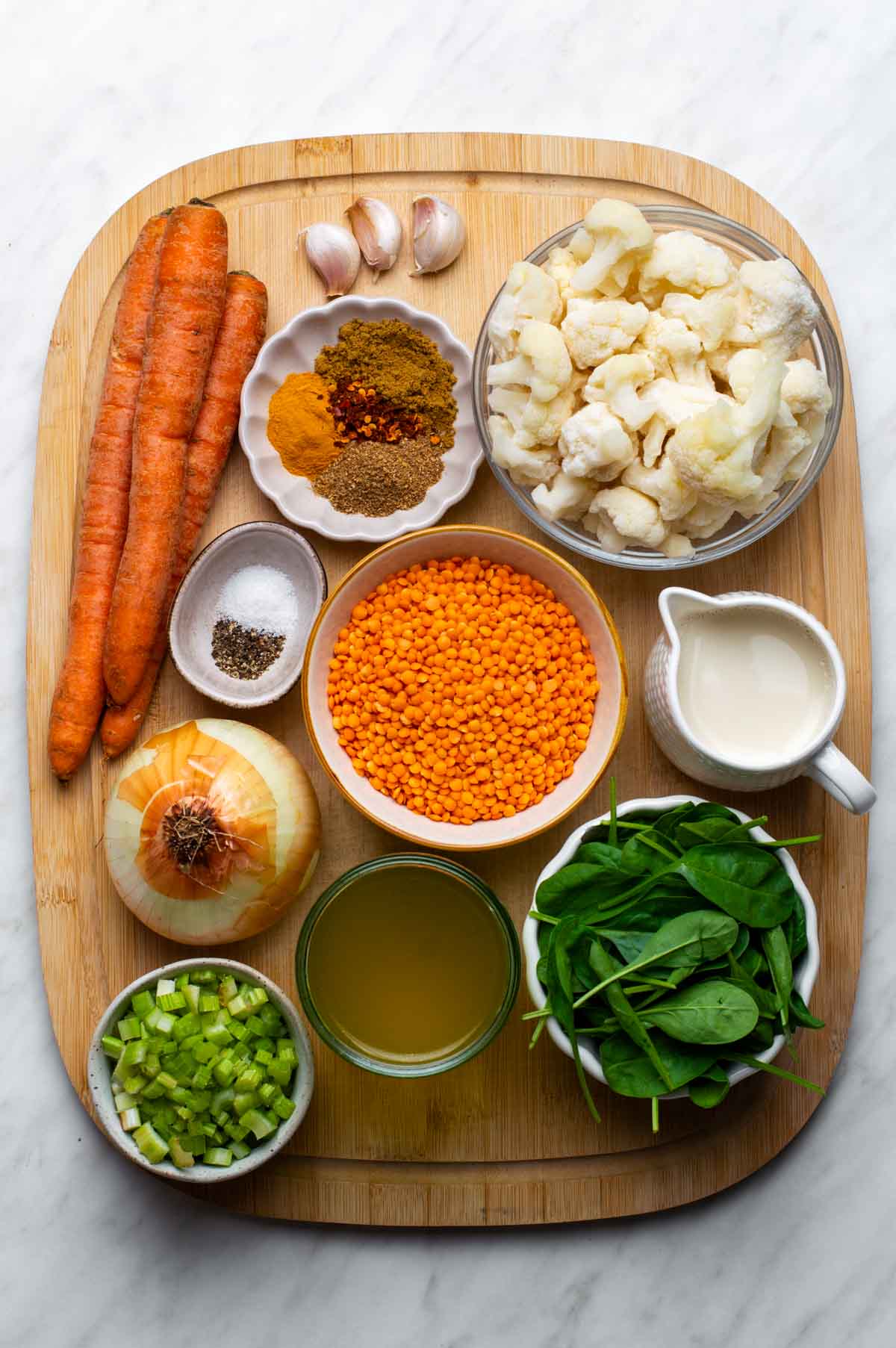 Fresh ingredients for cauliflower lentil soup arranged on a countertop, including cauliflower florets, dried lentils, carrots, celery, onions, garlic, and herbs.