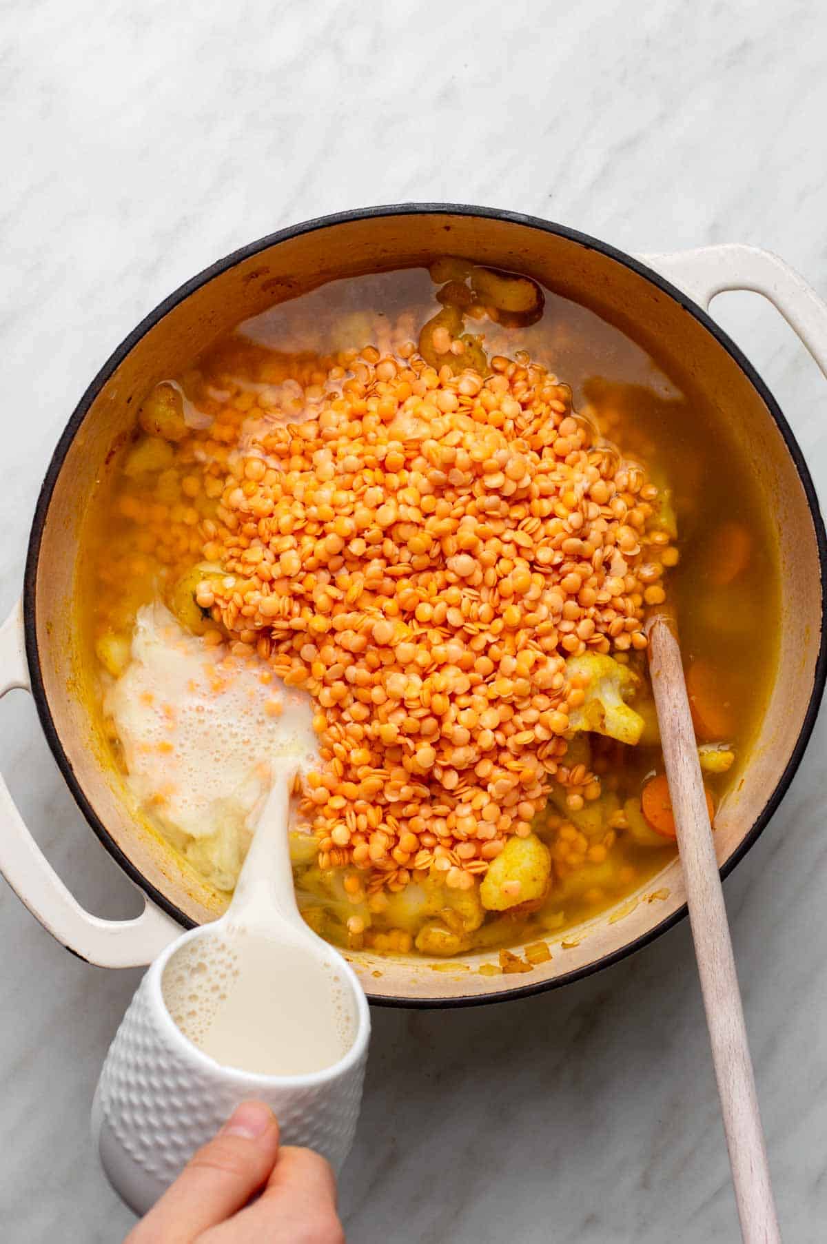 A mix of chopped vegetables, lentils, and seasonings for cauliflower lentil soup, with vegetable broth and almond milk added.