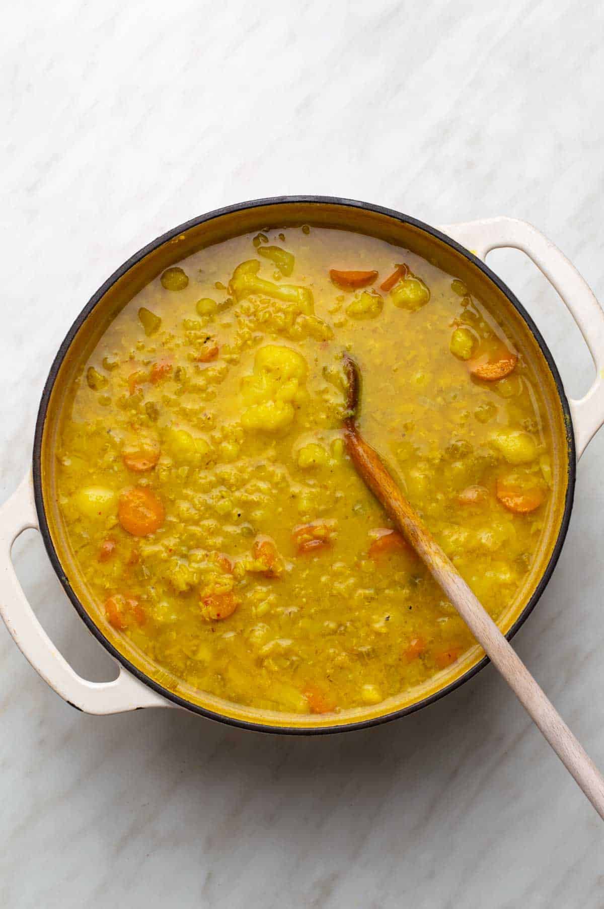 A mix of chopped vegetables, lentils, and seasonings for cauliflower lentil soup, with vegetable broth and almond milk added.