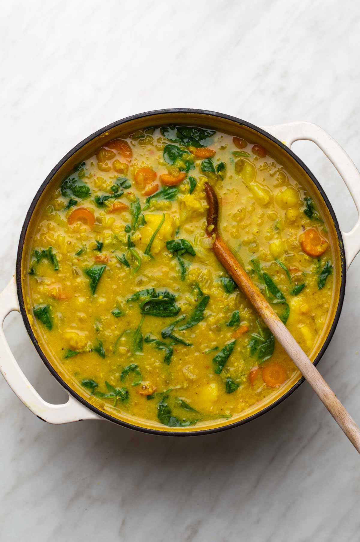 A mix of chopped vegetables, lentils, and seasonings for cauliflower lentil soup, with vegetable broth, almond milk, and fresh spinach added.
