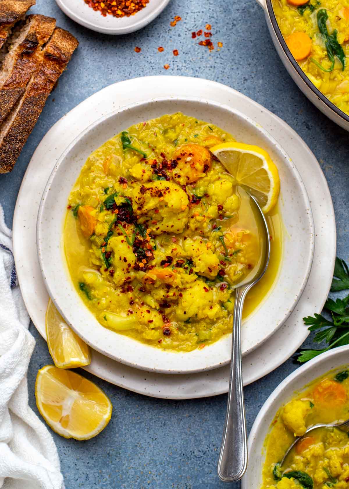 A bowl of cauliflower lentil soup with a spoon resting inside, topped with a slice of lemon.