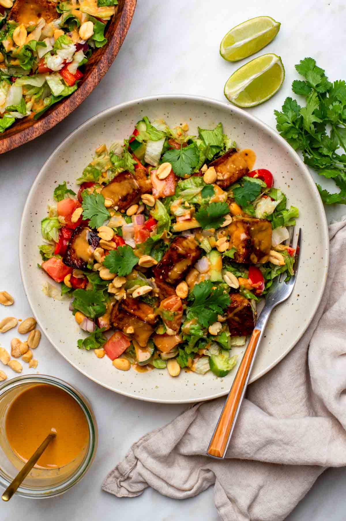 A bowl of Thai tofu salad with colorful vegetables, crispy tofu cubes, and fresh herbs, with a fork resting on the side.