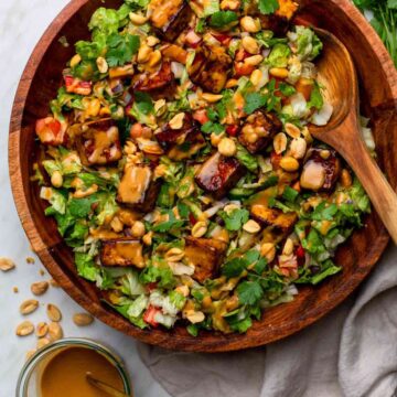 A bowl of Thai tofu salad with colorful vegetables, crispy tofu cubes, and fresh herbs, with a wooden spoon on the side.