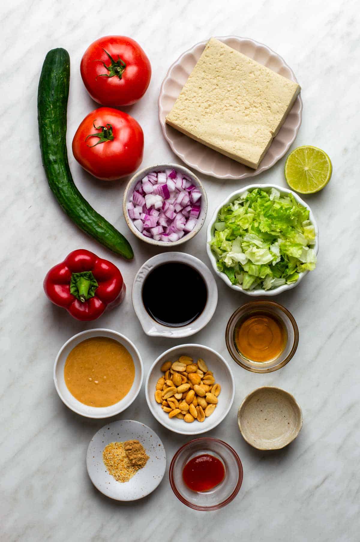 Fresh ingredients for Thai tofu salad arranged on a countertop, including tofu, colorful vegetables, fresh herbs, and a small bowl of dressing.