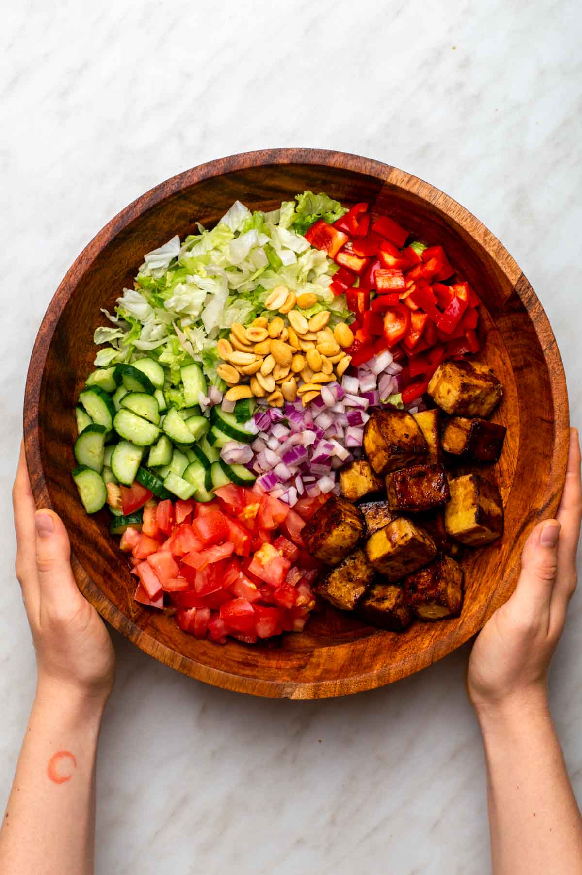 A bowl filled with chopped ingredients for Thai tofu salad, including colorful vegetables, herbs, and tofu.