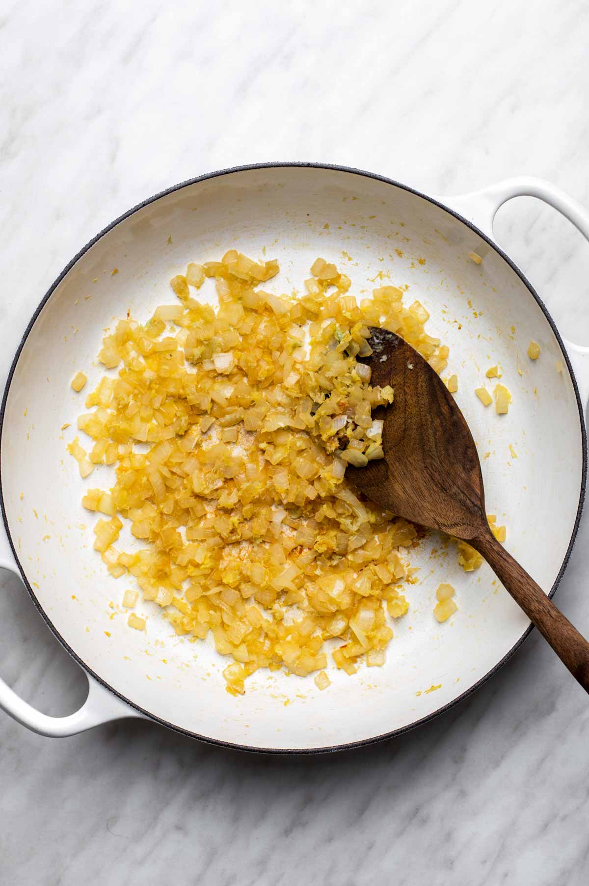Onion, garlic, and ginger sautéing in a pan with a splash of vegetable broth until soft and fragrant.