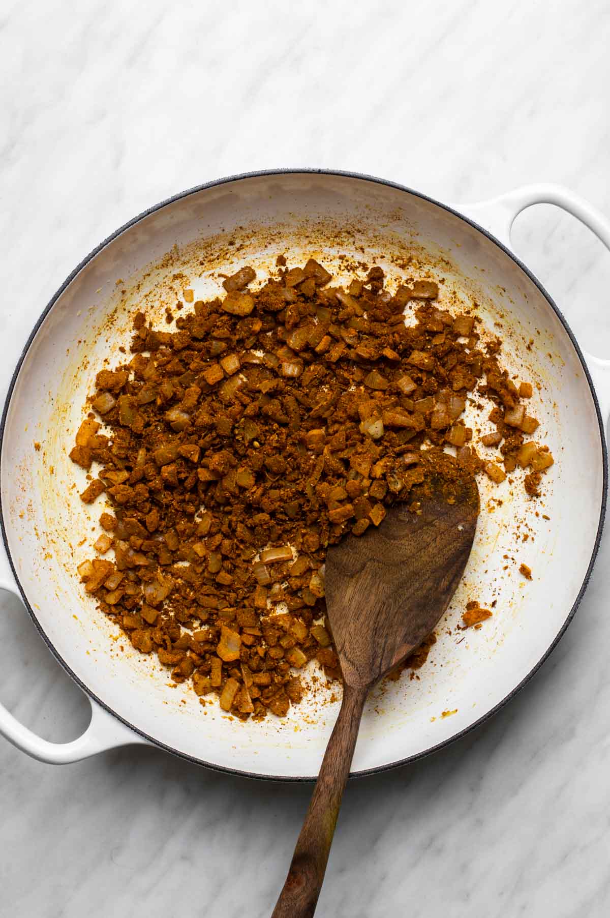 Curry powder, cumin, coriander, turmeric, and cayenne being stirred into sautéed aromatics in a pan to toast and release their flavors.