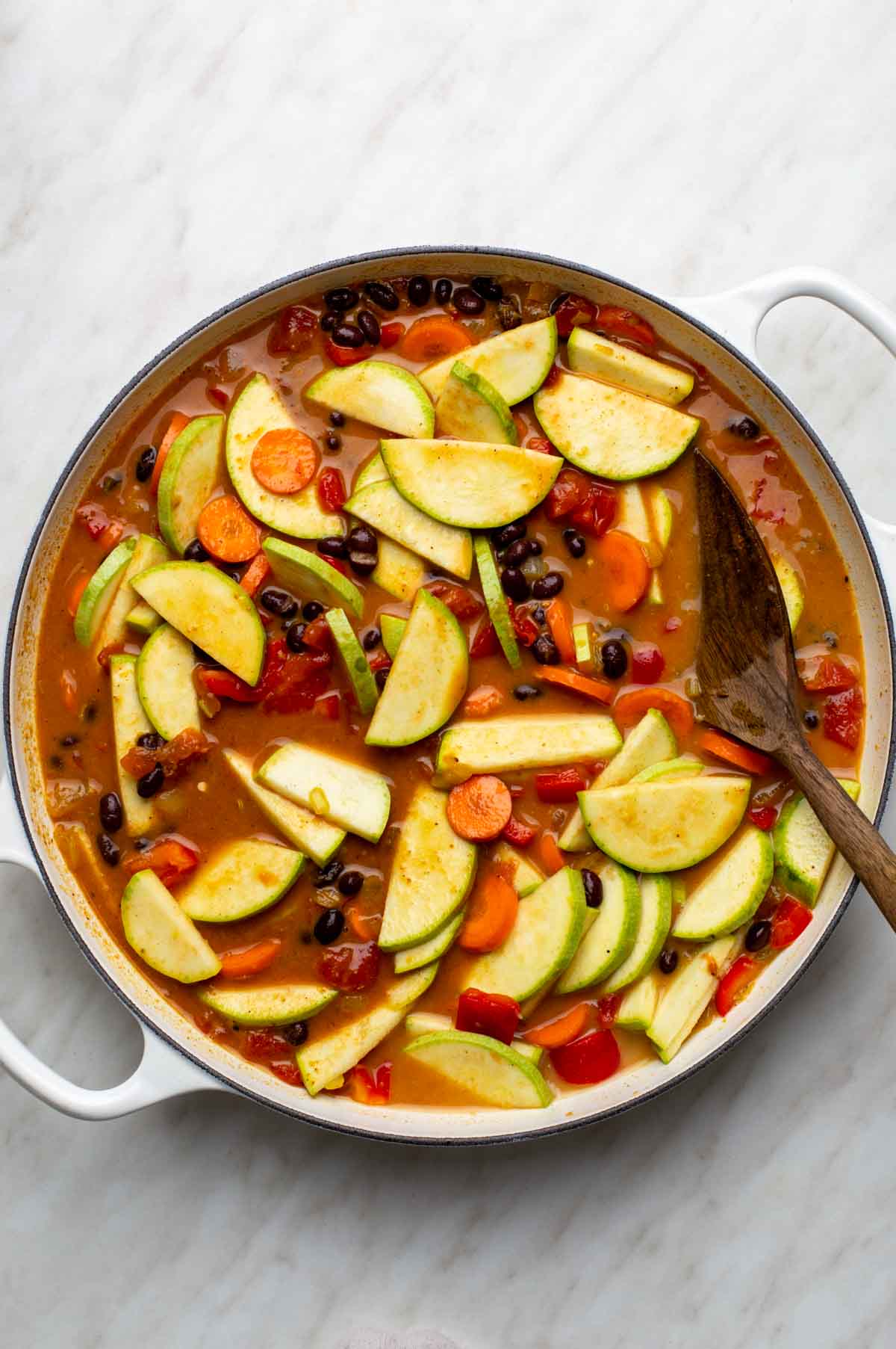 Diced tomatoes, black beans, coconut milk, and broth simmering with vegetables in a pan until tender and thickened into curry.