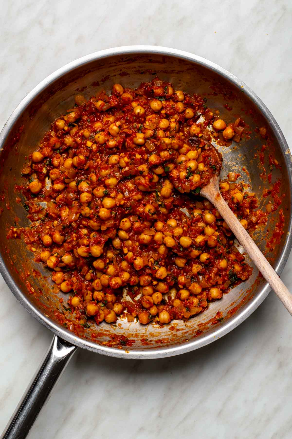 Chickpeas, vegetable broth, marinara sauce, and crushed red pepper flakes being stirred in a pan, with fresh basil added.