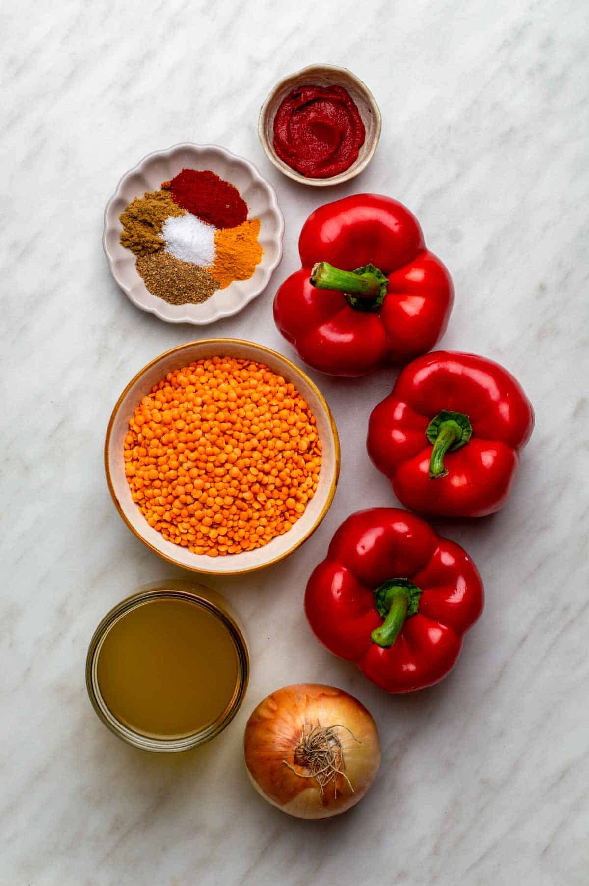 Fresh ingredients for lentil red pepper soup arranged on a surface, including lentils, red peppers, onions, garlic, and spices.