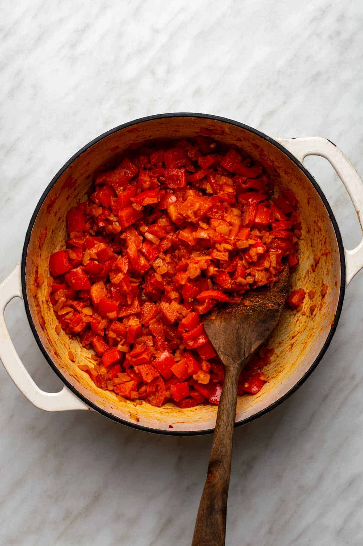 Diced bell peppers and onions cooking in a large stockpot, seasoned with salt and black pepper.