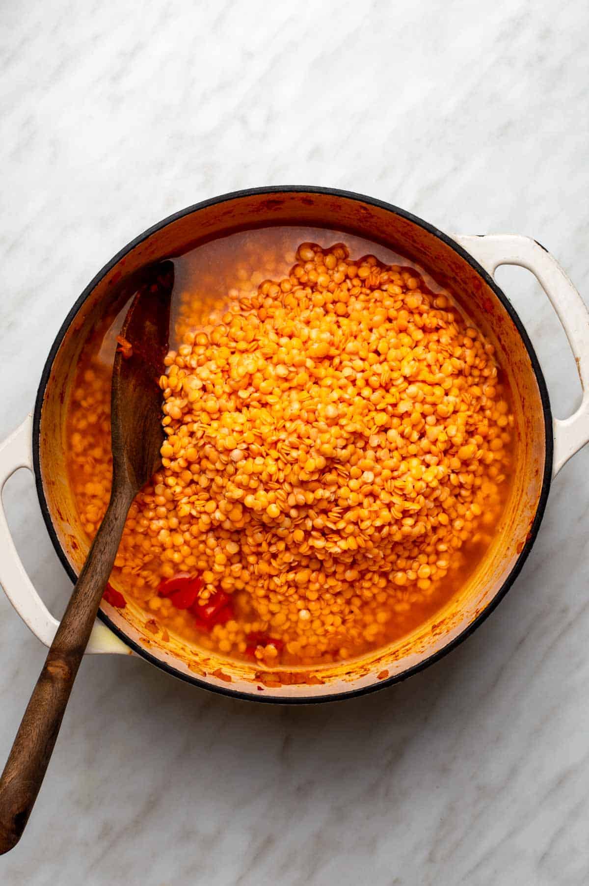 Diced bell peppers and onions in a large stockpot being stirred with tomato paste, smoked paprika, cumin, coriander, and turmeric.