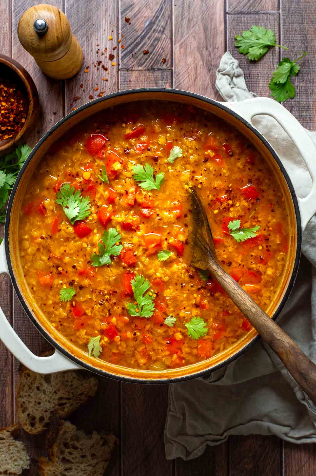Large stockpot filled with diced bell peppers, onions, tomato paste, spices, vegetable broth, and red lentils being stirred together.