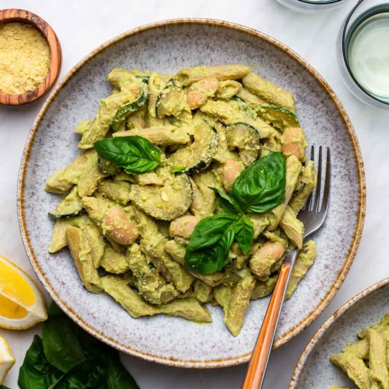 Creamy vegan zucchini pasta on a plate with a fork, topped with fresh herbs.