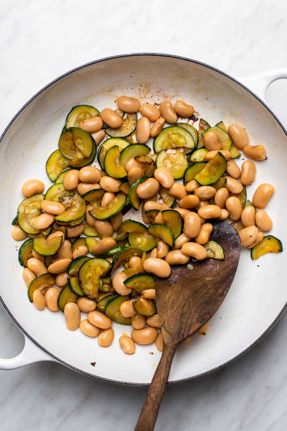 Zucchini slices sautéing in a pan with beans added.