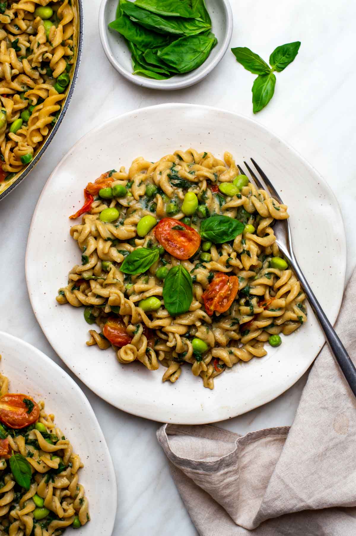 Creamy veggie pasta on a plate topped with herbs and a fork on the side.