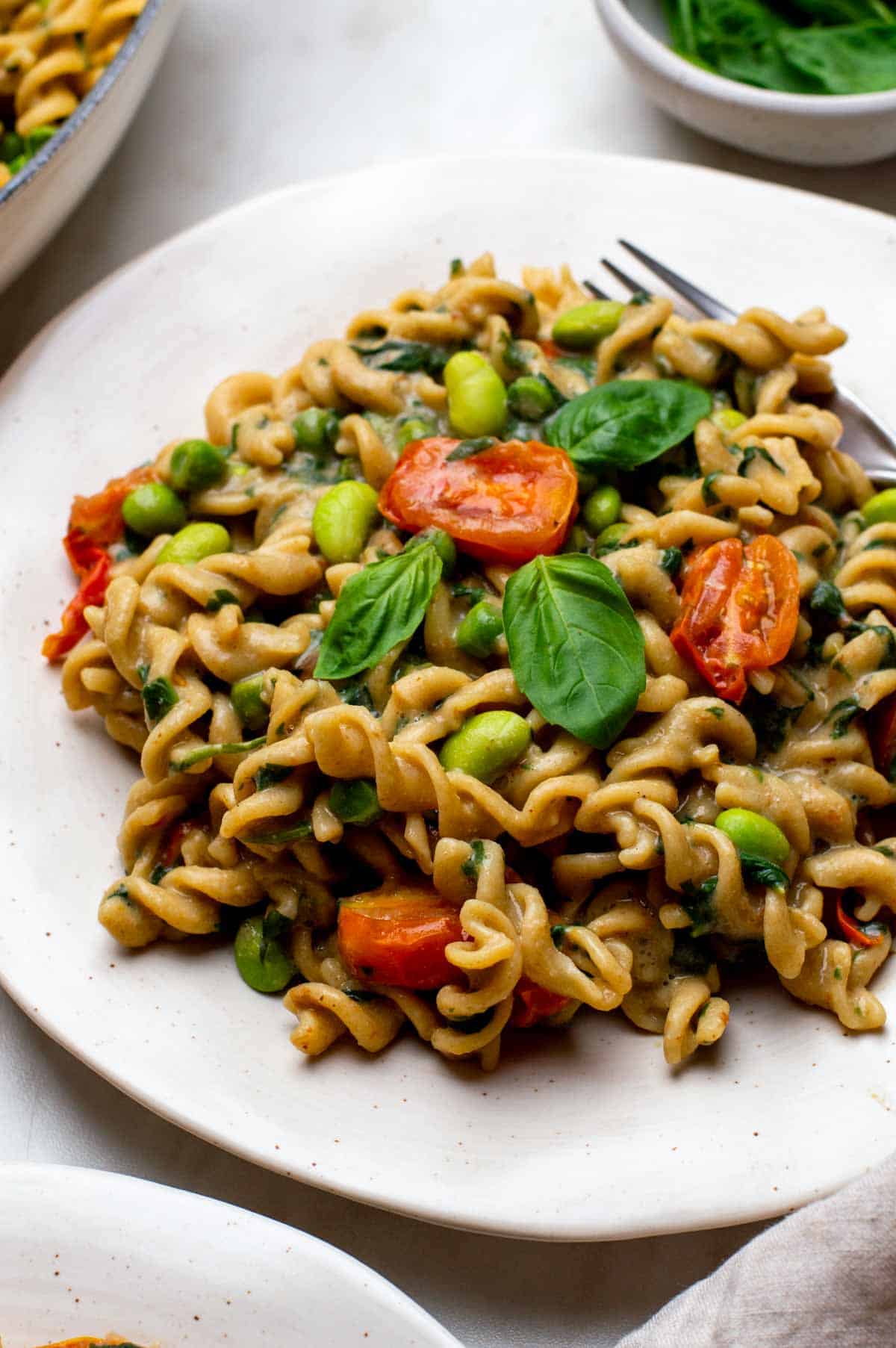 Creamy veggie pasta on a plate topped with herbs and a fork on the side.