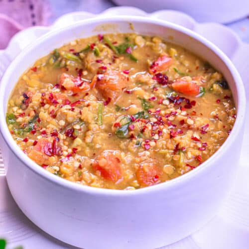 A bowl of hearty red lentil and spinach soup with a rich, golden-orange color.