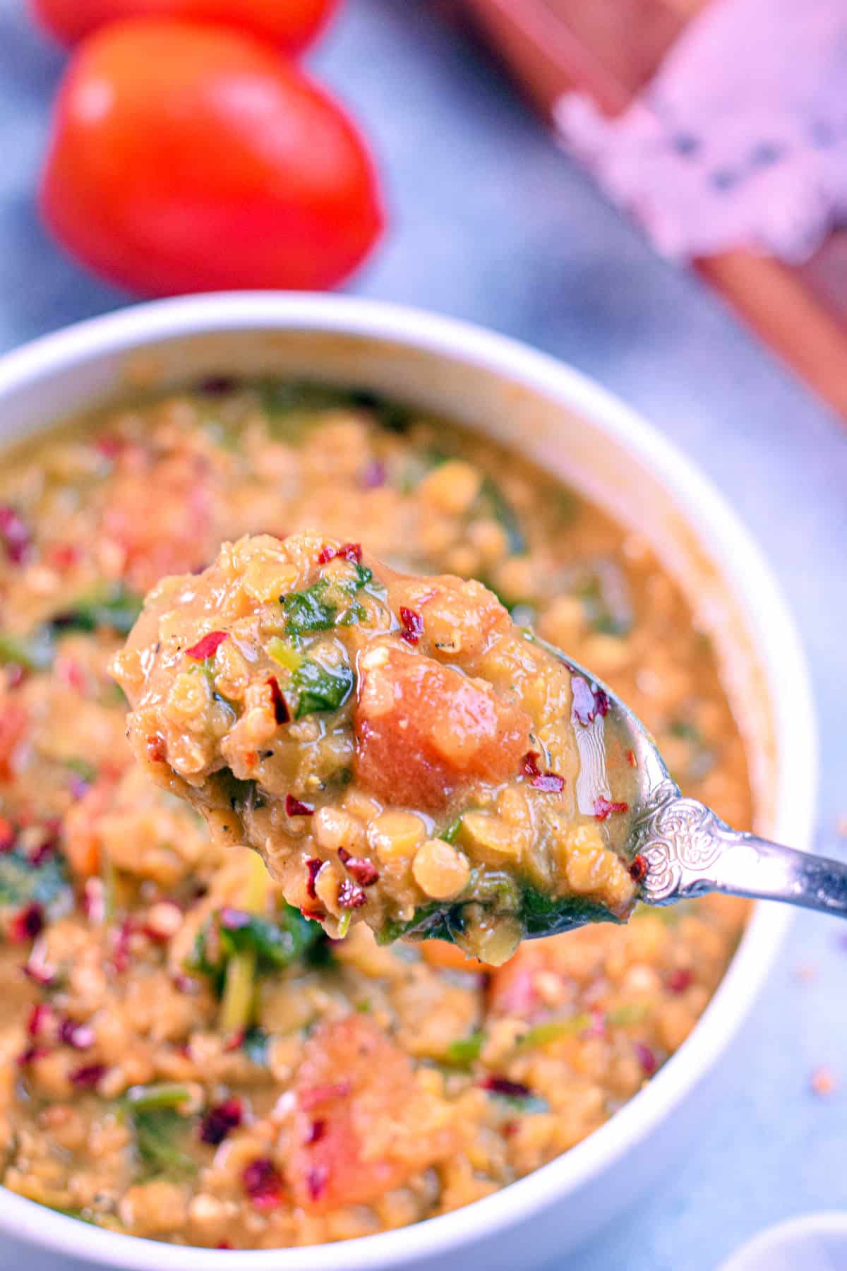 A spoon lifting red lentil and spinach soup from a bowl.