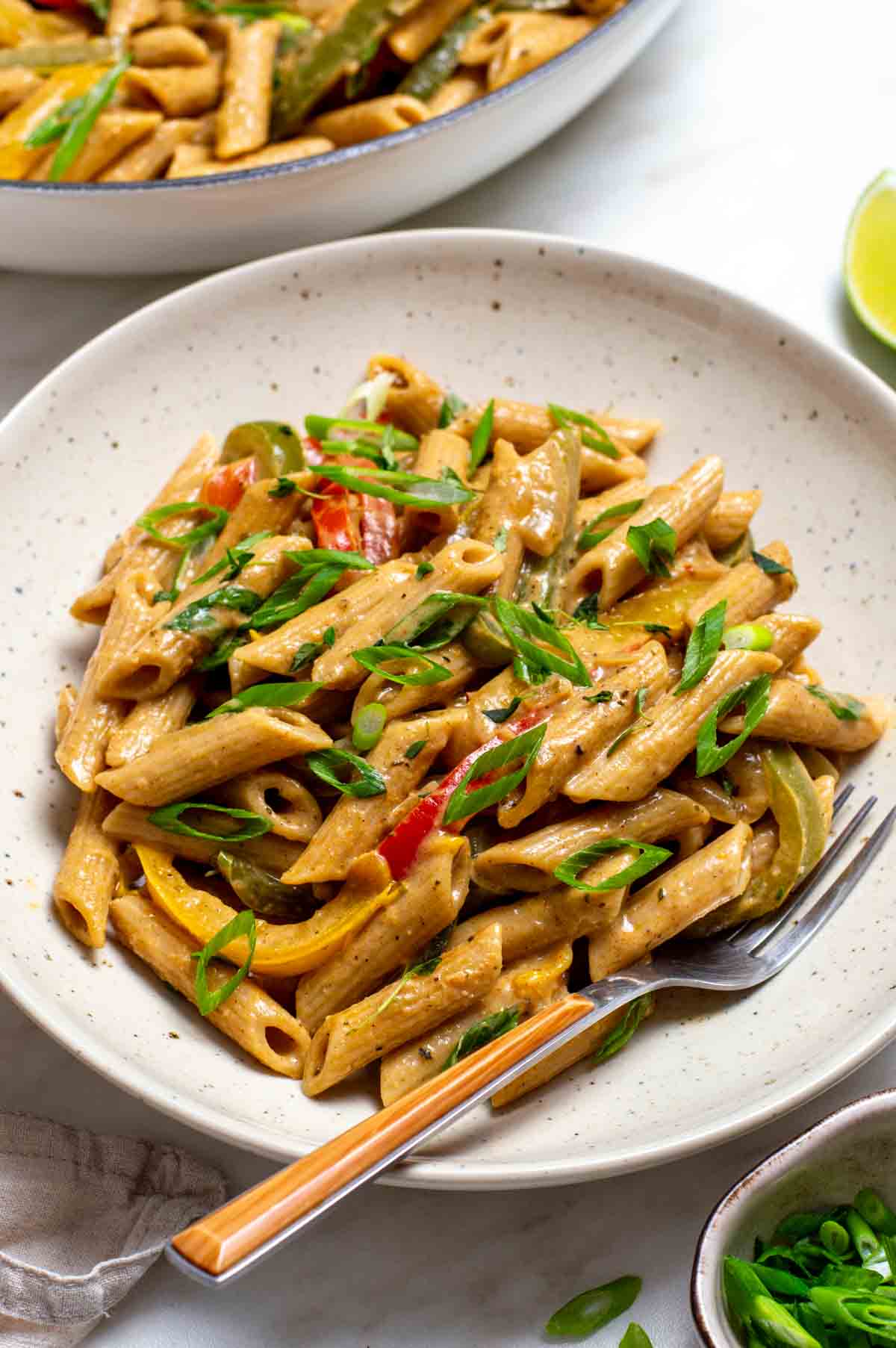 A plate of colorful vegan Rasta Pasta with creamy sauce and bell peppers, served with a fork on the side.