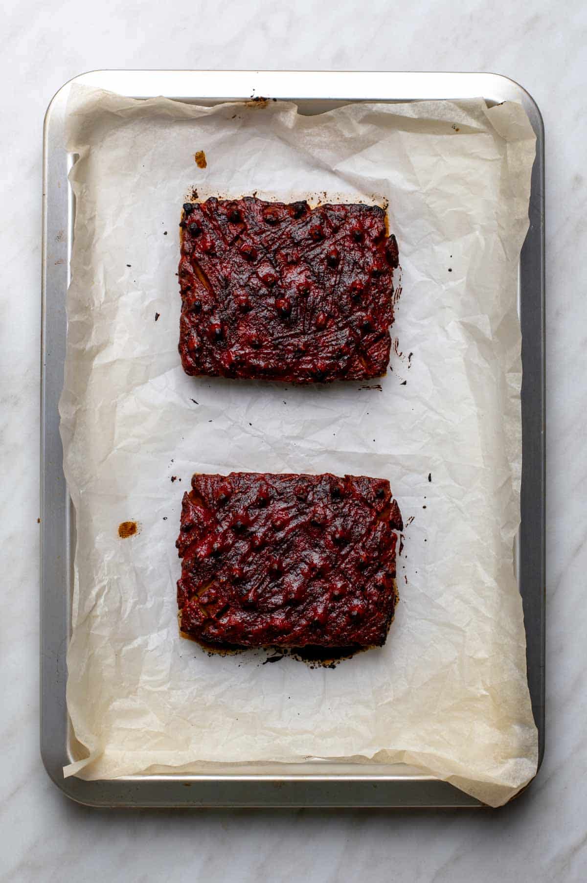 Two baked squares of glazed vegan ham cooling on a parchment-lined baking sheet.
