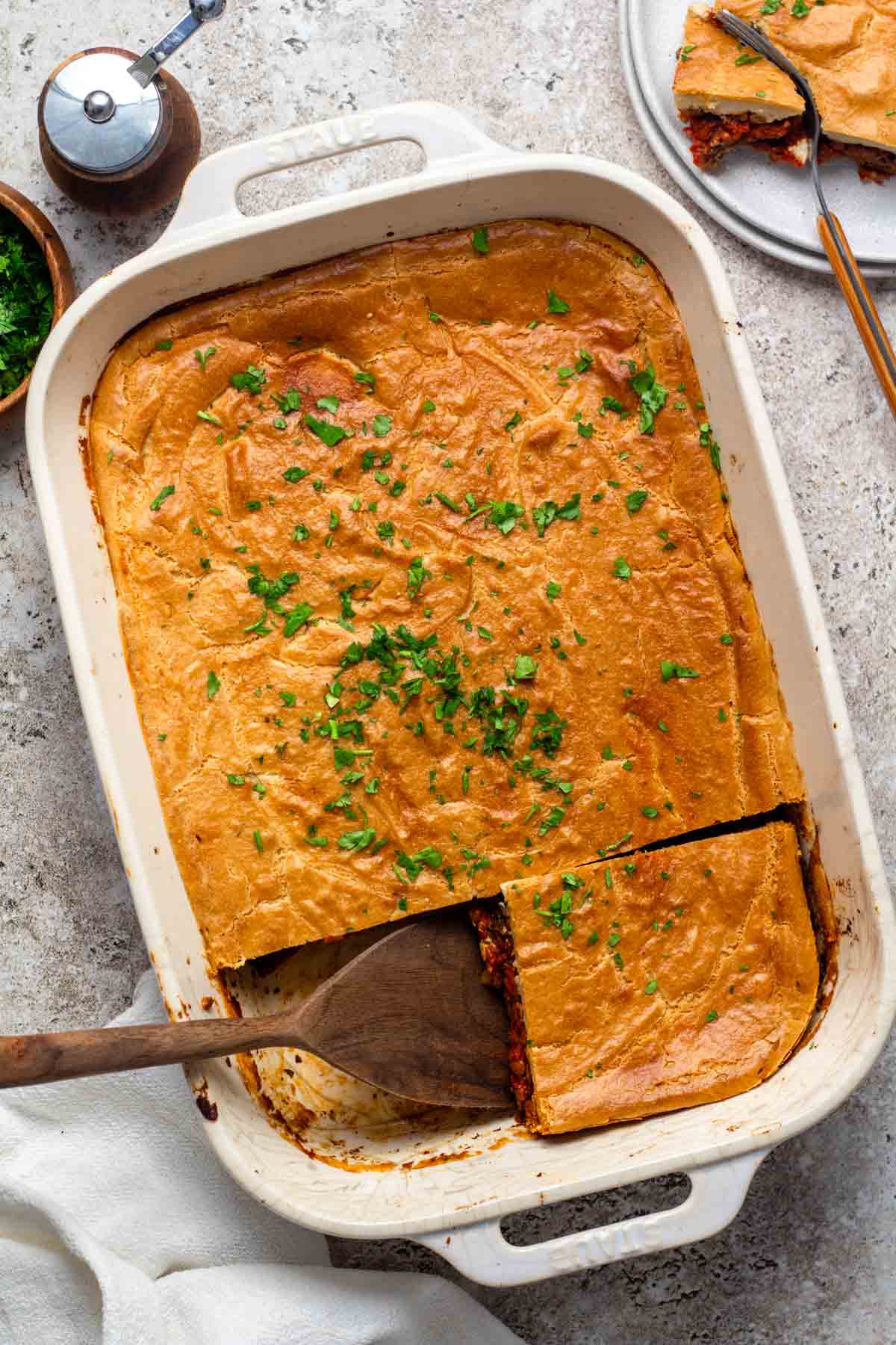 Sliced freshly baked vegan moussaka in a white baking dish with a golden, creamy cashew béchamel top.