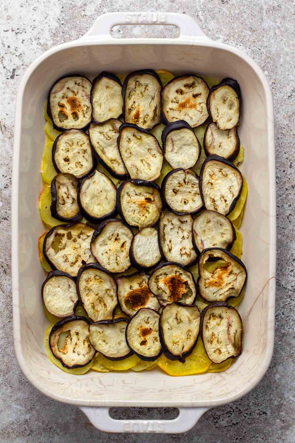 Roasted eggplants above the roasted potatoes in a baking dish.