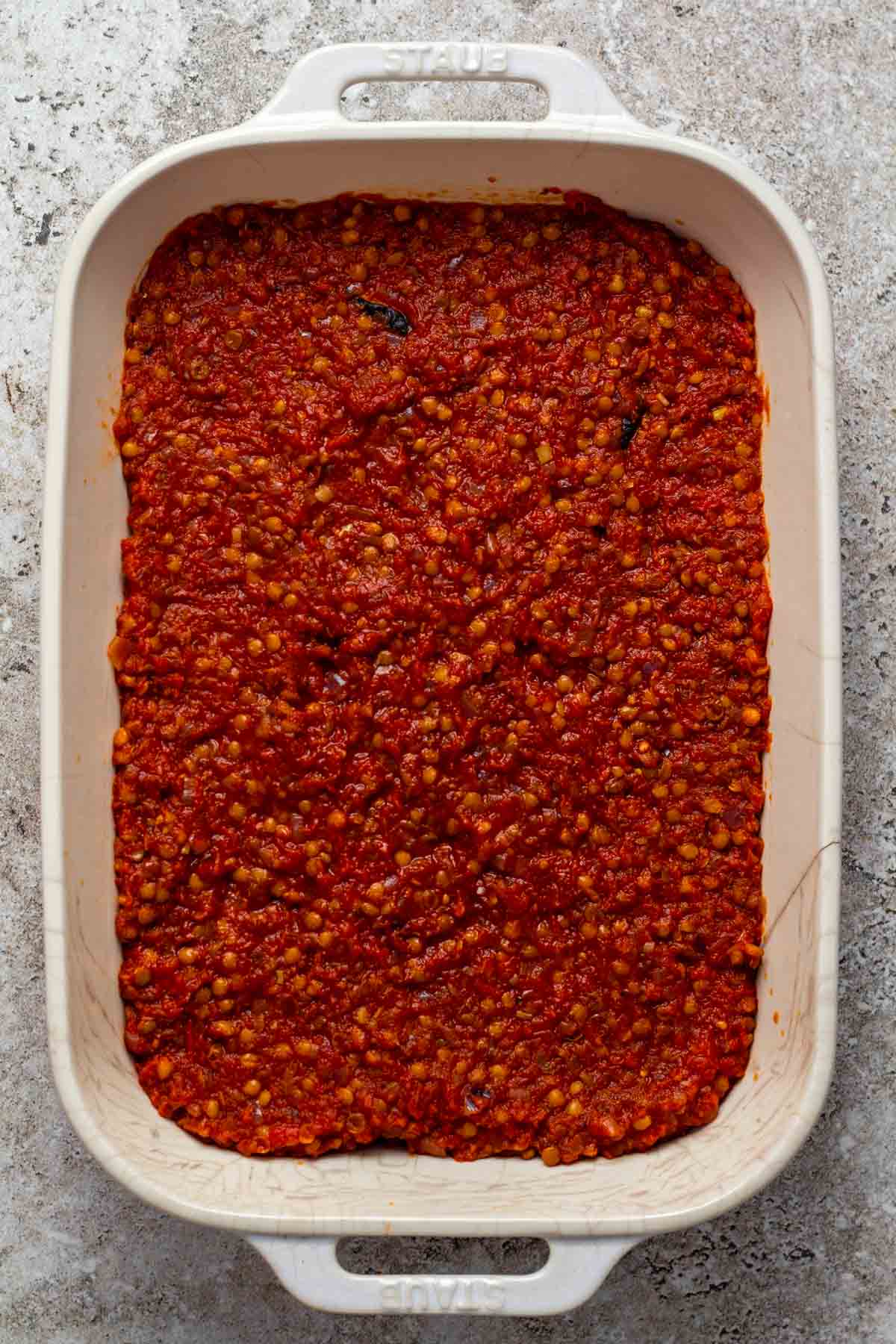 Tomato lentil spread on the roasted vegetables in a baking dish.